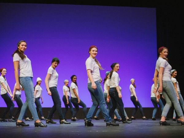 Dancers performing on stage with purple background.